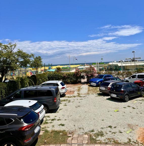 Parkplatz in Strandnähe mit Autos und bunten Sonnenschirmen.